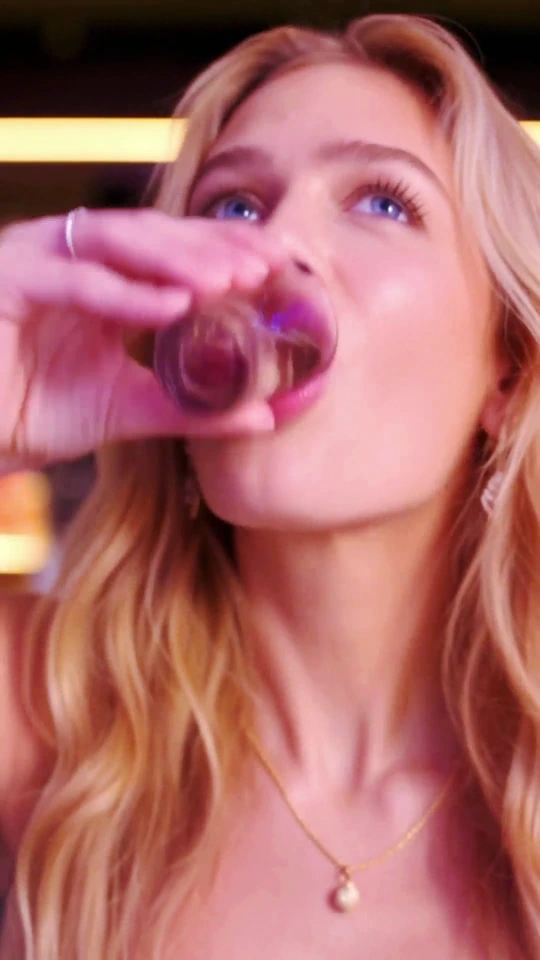 A woman raising a shot glass in a purple-lit nightclub